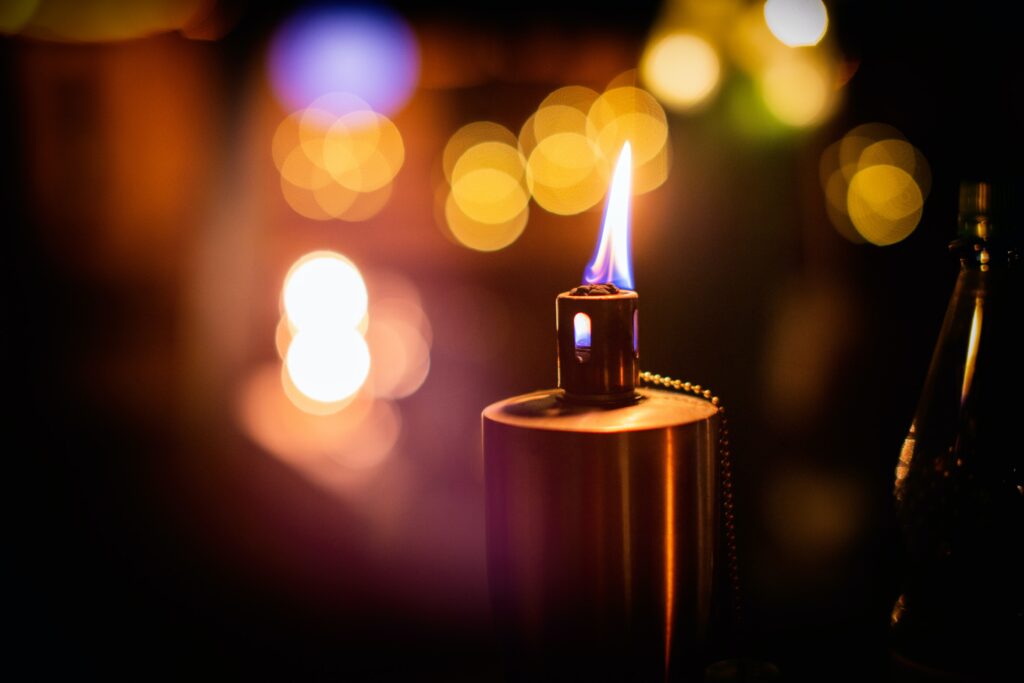 closeup of a lit torch with a small flame and blurred string lights in the background 