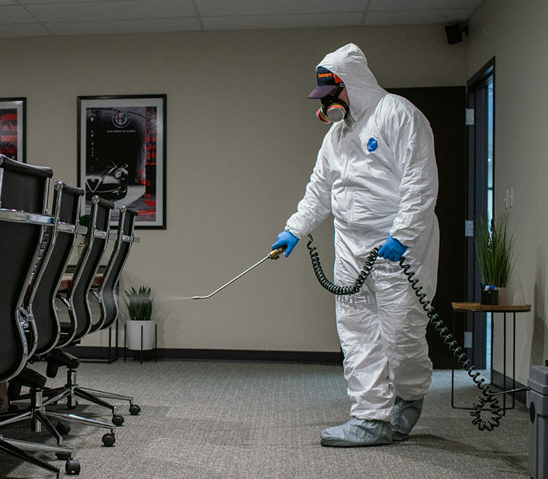 Catseye technician in hazmat suit disinfecting an office with sprayer to conduct Catseye's Viral-Guard service