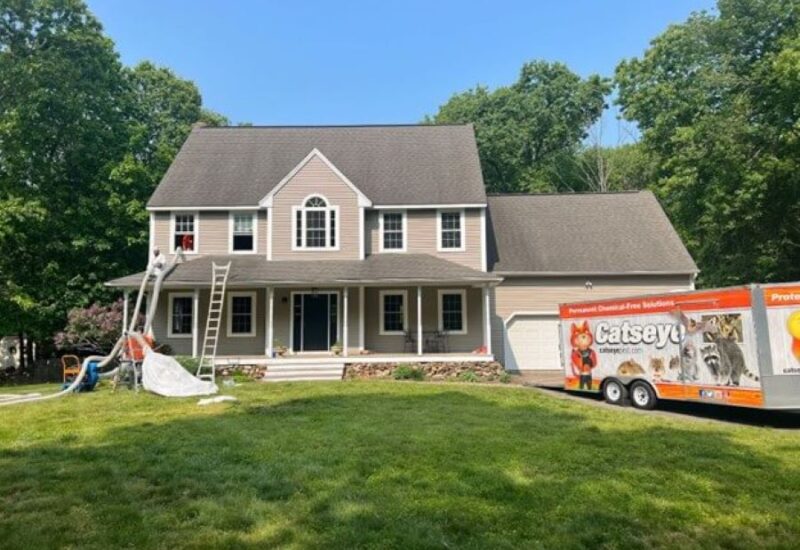 a two-story house in Connecticut with a Catseye Pest Control trailer in the driveway with ducts coming out of the second story to treat bat bugs