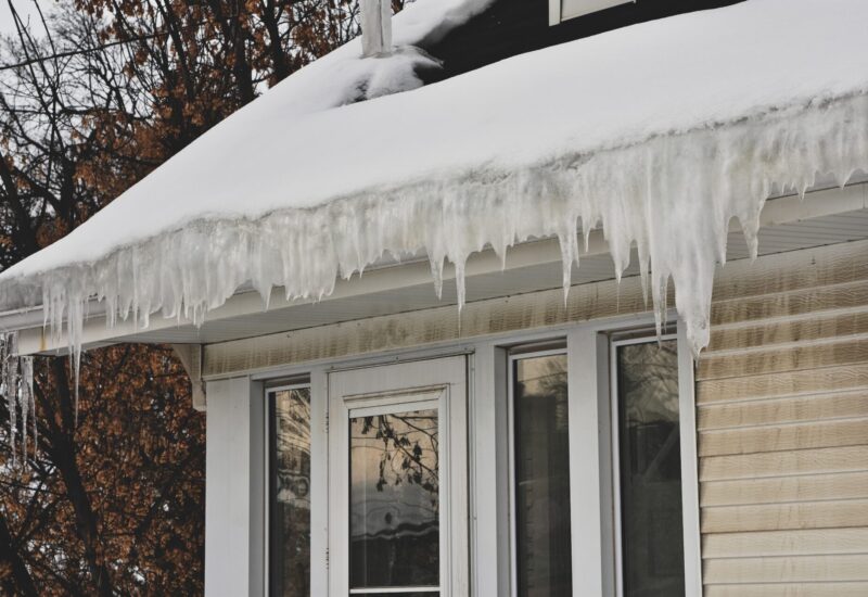 winter ice dam caused by melting slow; icicles hanging along the gutters of a home with beige siding