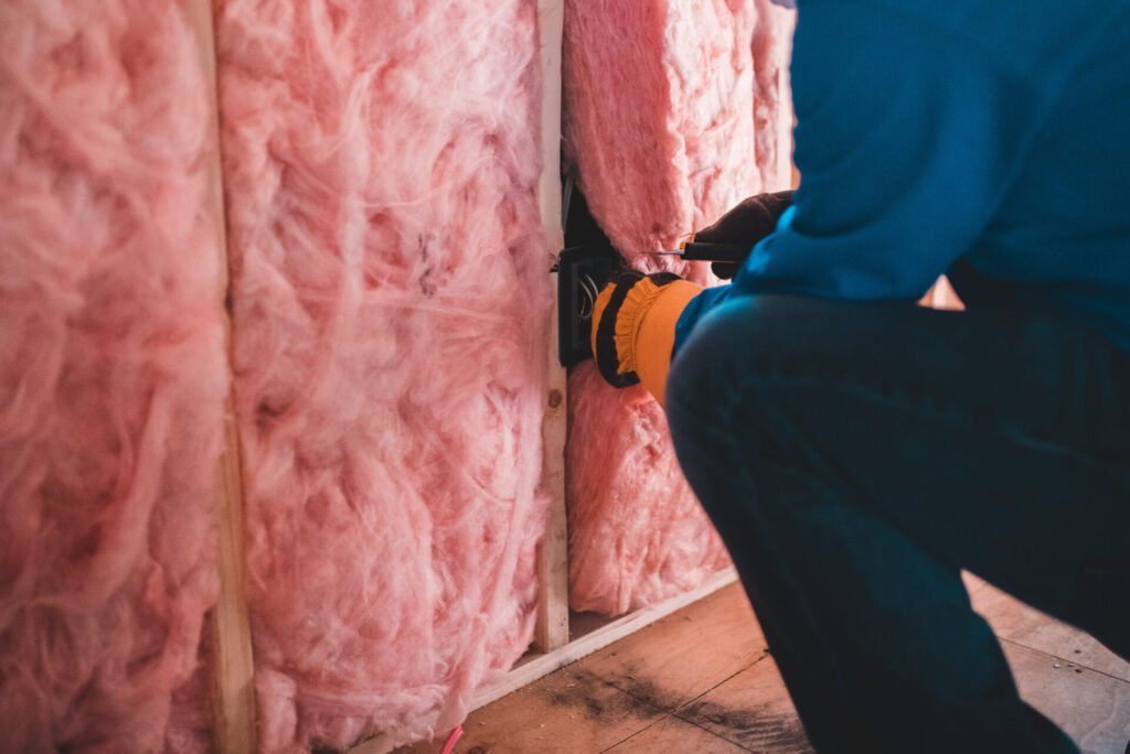 worker in dark blue coveralls and orange gloves installing pink insulation